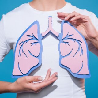 kobieta w białej koszulce na niebieskim tle trzymająca w ręku papierowy model płuc